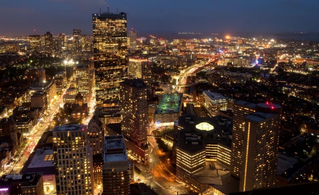 an aerial view of Boston city at night with multiple lights lighting up the buildings, an example of what you can see during Boston trips