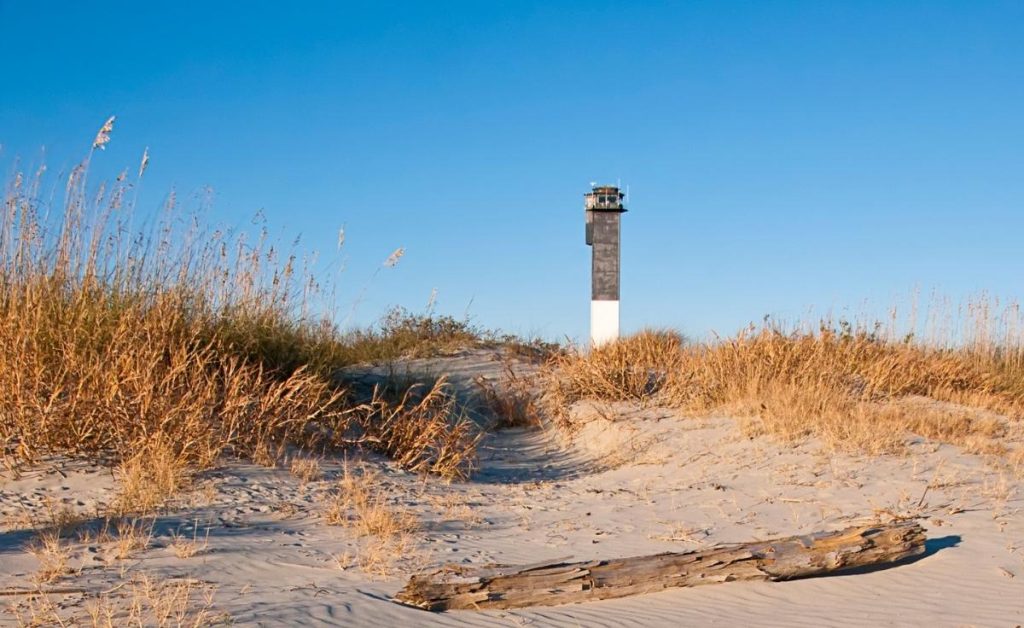 the beach and sea grass at Sullivan's Island with an old lighthouse in the background in Charleston, South Carolina