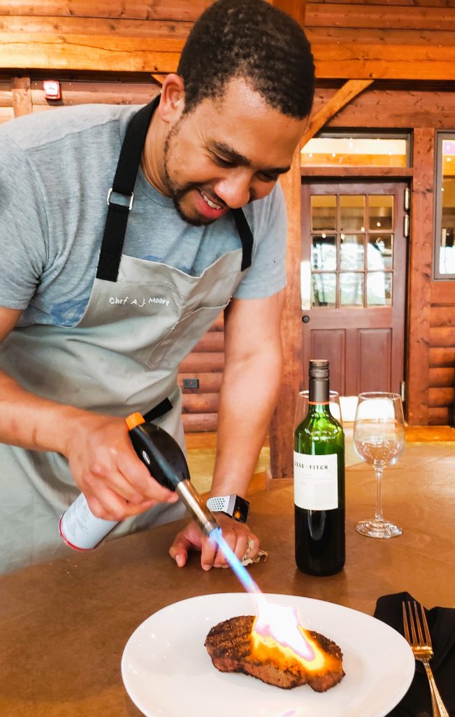 Chef AJ Moore plays with fire-literally- flambe a steak on a wooden table   © Jo Clark