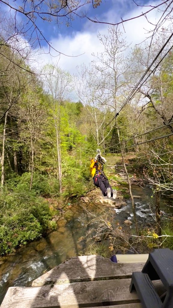 Writer Jo Clark coming in on the zipline over a creek with rocks and green trees © Jo Clark