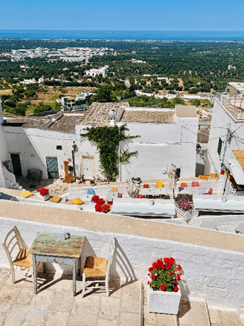 Borgo Antico Bistrot a restaurant in Ostuni Italy with light blue skies and an aerial view of Ostuni town with white buildings, red flowers and chairs