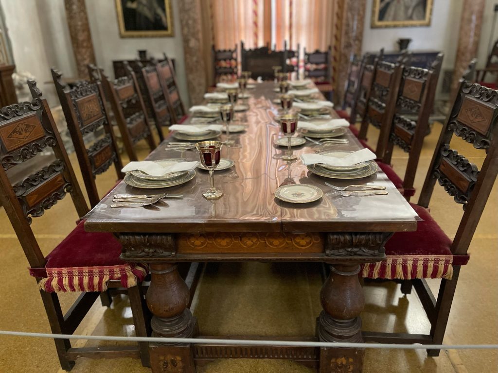 castles in Florida Vizcaya with a dark dining room table, chairs with red cushions, white tablesetting for 10, napkins on top of bowls. Room has white walls trimmed in a gold color