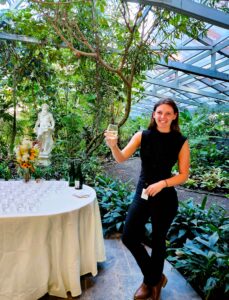 Greeter in Magnolia Plantation and Gardens Conservatory, holding out a stemless Magnolia Plantation signature glass of champagne.
