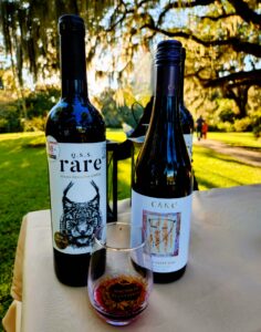 Sample glass of red wine in front of two bottles that hold Rare and Cake wines