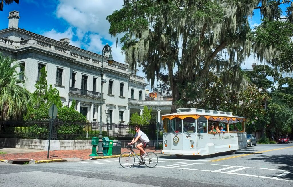 Trolly car stopping for a biker to cross a street. A Trolly tour is a perfect way to discover Savannah