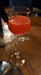 A red drink in a rose-shaped glass with leaves on the stem.