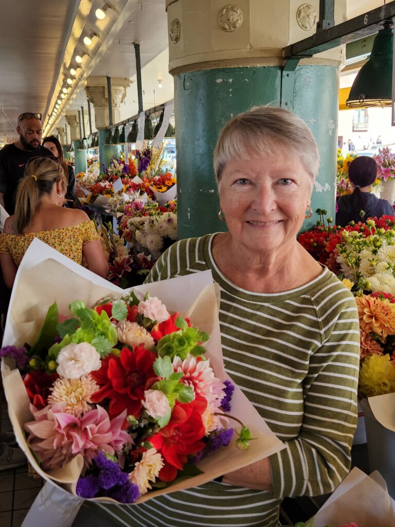 Writer Jo holding a huge bouquet of fresh flowers in a market filled with flowers
