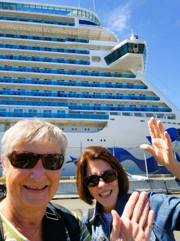 Two women waving goodbye boarding Princess Alaskan Cruise with Discovery towering in the background