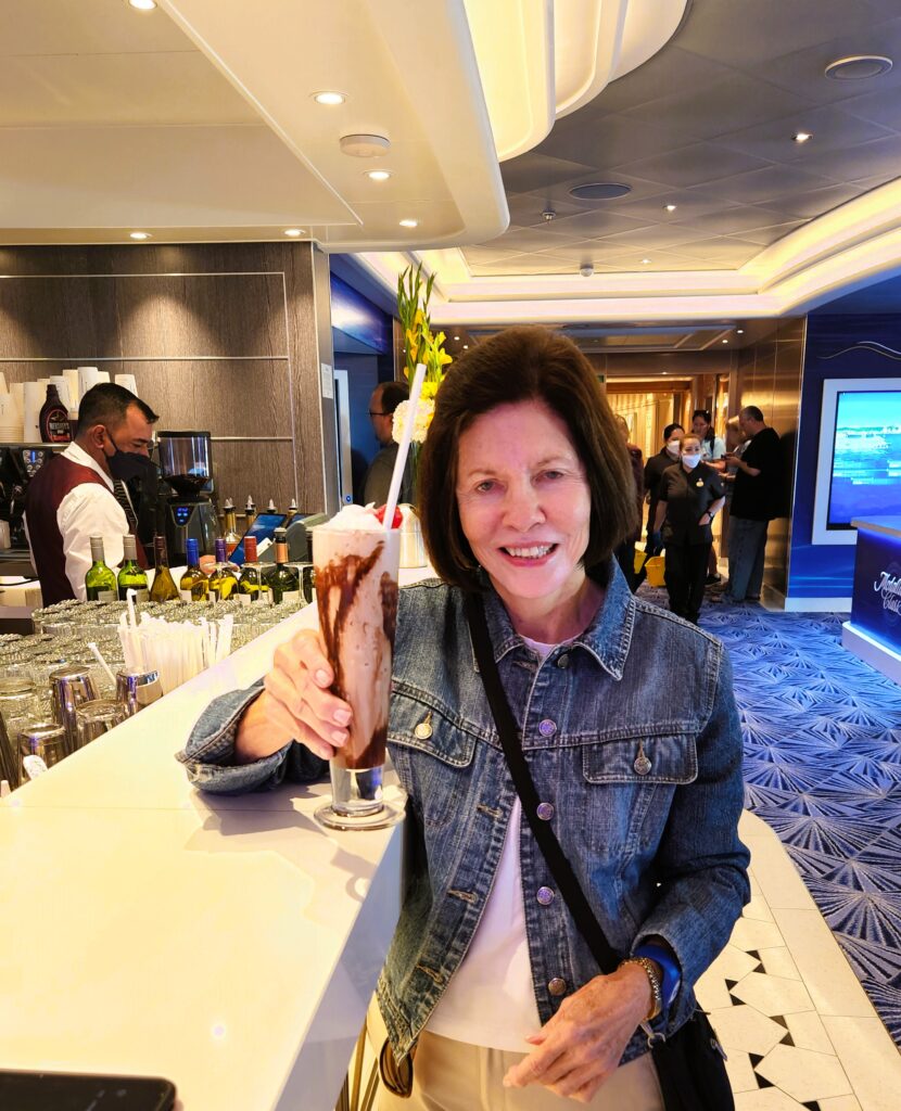 Smiling woman holding a glass with the mudslide drink, and bar and bartender in the background.