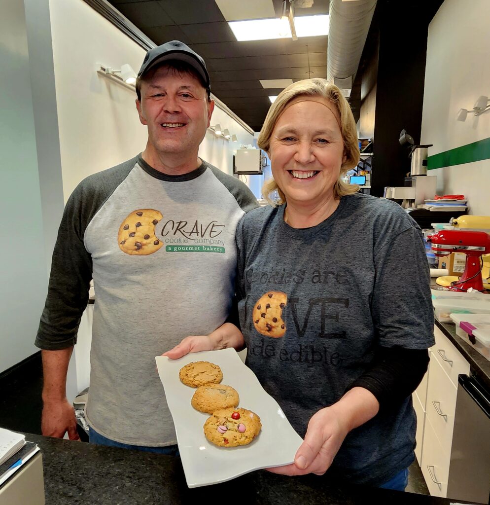 Man and woman (owners) in Crave Cookies holding a plate of three perfectly beautiful cookies