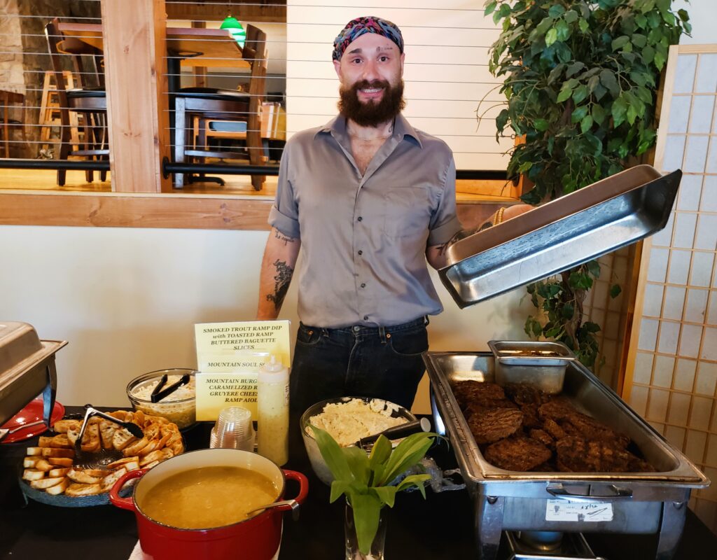 Chef at table of ramp burgers, ramp soup in red Dutch Oven