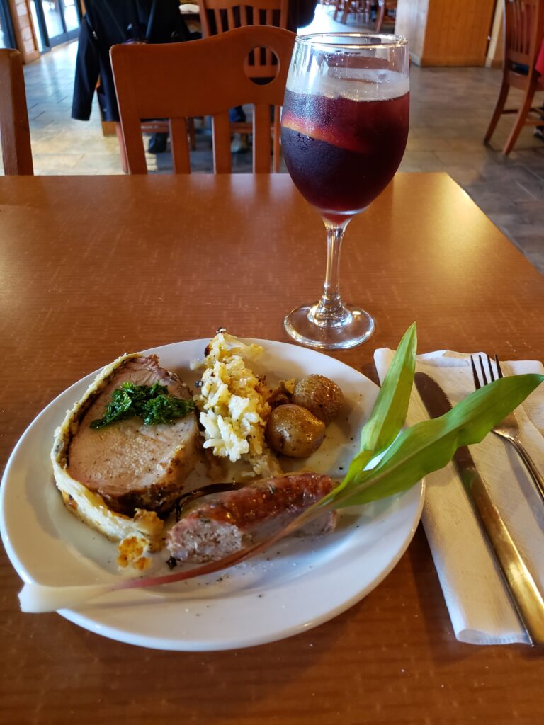 A plate filled with potatoes, sausage, and pork Wellington, and a glass of red wine 