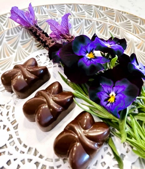 Intricate designs on dark chocolates from Chocolate Tofino, on a plate with live purple pansies