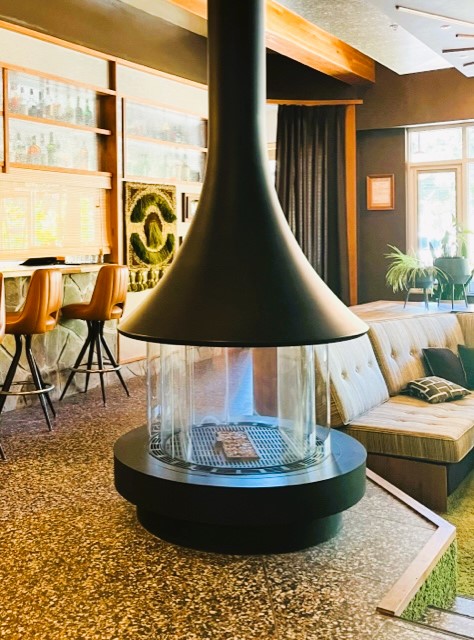 A retro-style mid-century sunken living room with a round metal floor to ceiling fireplace