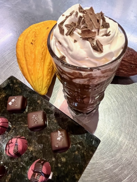 Fancy cut glass filled with hot chocolate elixir, and a plate filled with fine chocolates, and yellow cacao pod
