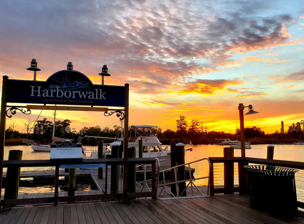 Pink and Golden sunset skies over the Sampit River in Historic Georgetown SC, viewed from in front of the Harborwalk sign, boats docked.