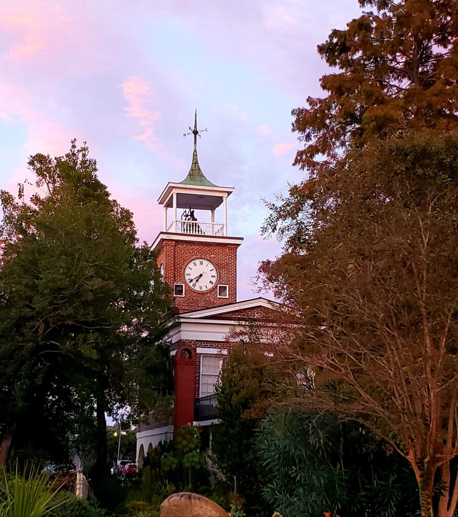 Historic Georgetown SC Town Clock, in a brick tower ove the market, surrounded by trees, and with the pink and blue sky of the early sunset.