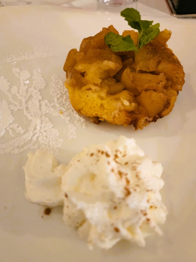 Serving of Upside-Down Apple Crumble with Cream on the side on a white plate.