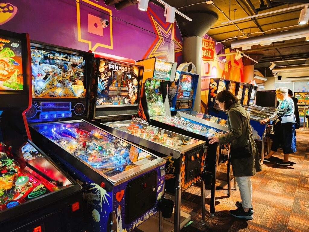 Two women play pinball machines, unfortunately they are not scoring!