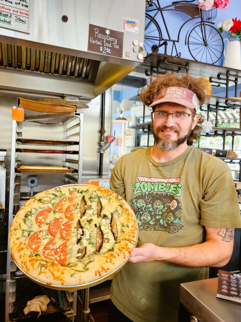 Baker at On the Rise Bakery shows off a half-and-half pizza of tomatoes and zucchini.