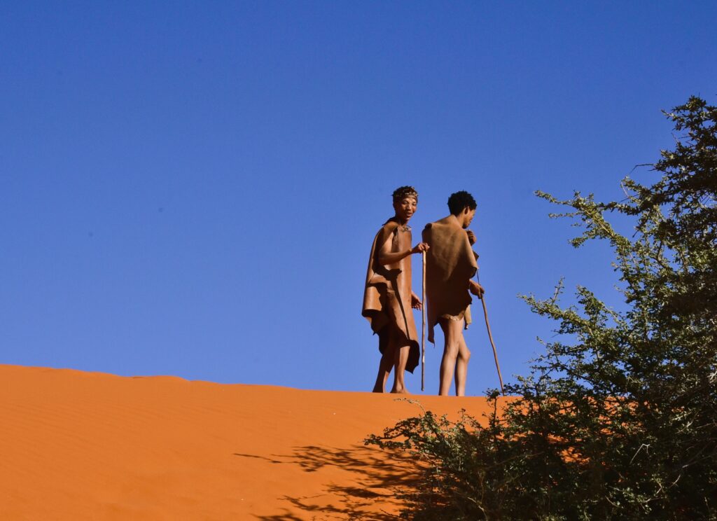 Two Koi-San tribal members walking along the top of a red dune in Namibia.