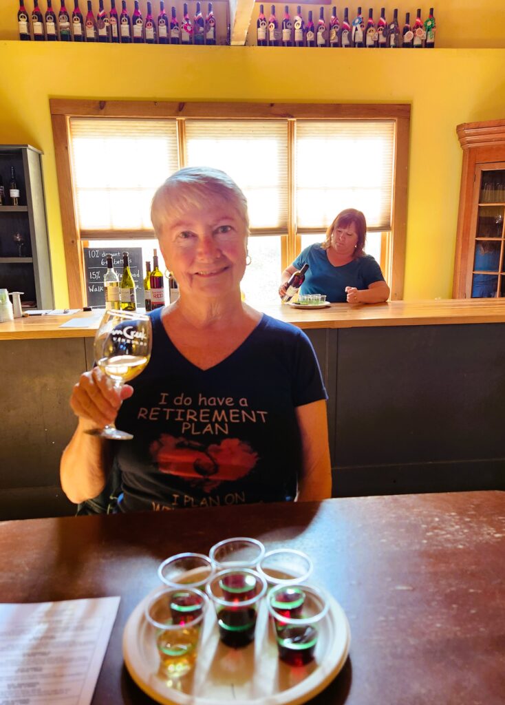 Writer Jo Clark wearing a favorite t-shirt and drinking wine at Elkin Creek. The shirt says, "I have a retirement plan, I plan on tasting wine!"