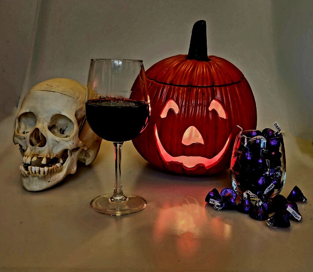 Halloween Candy Wine Pairings are red wine and chocolate kisses set in a scene between a skull and jack-o-lantern.