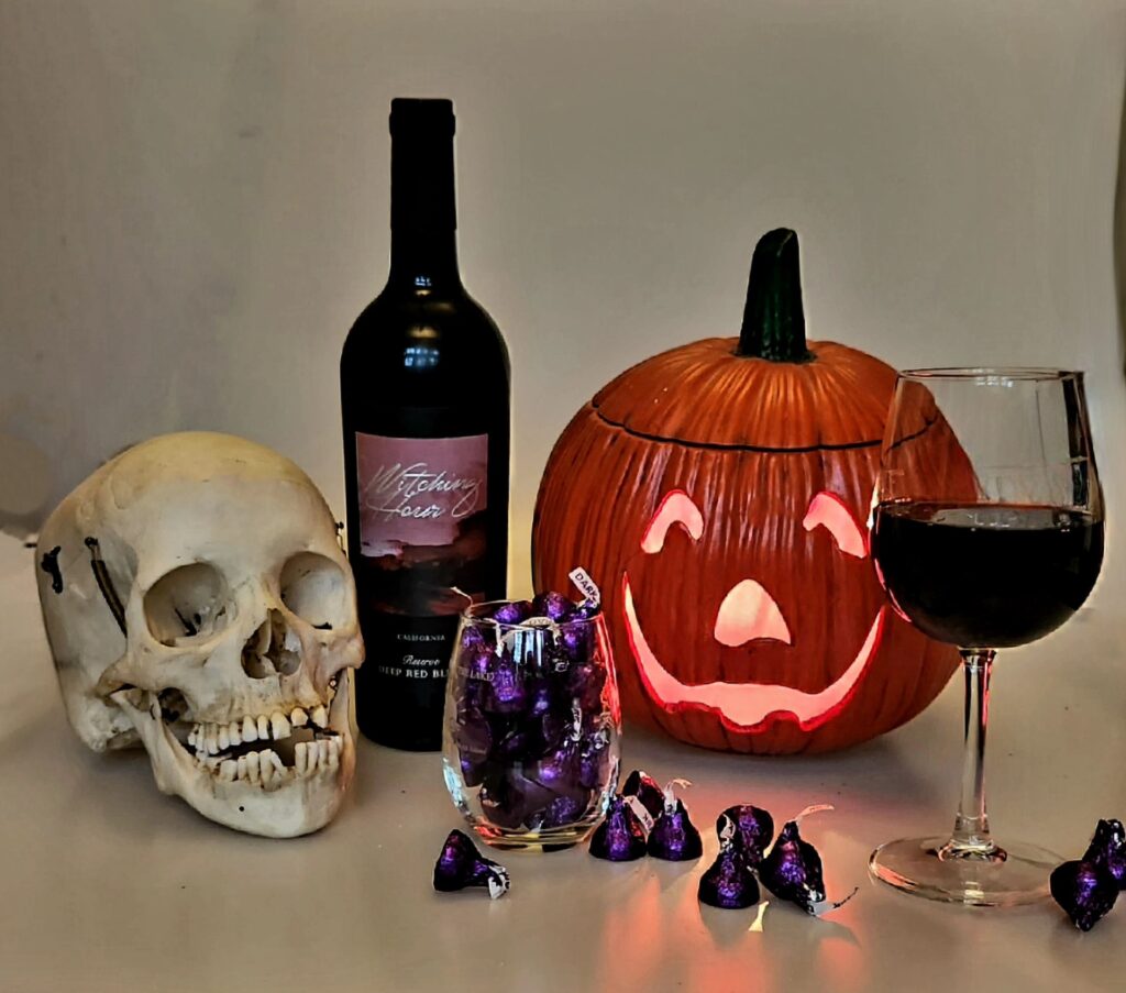 Bottle of Witching Hour Red Blend wine and chocolate kissess - with a skull, glass of  Red Wine, and a stemless glass of kisses.