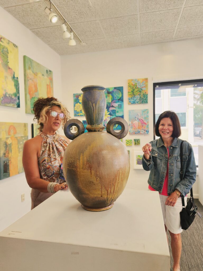 Twh women admiring a large pottery vase, with rounded "belly" and two large round rings for handles.