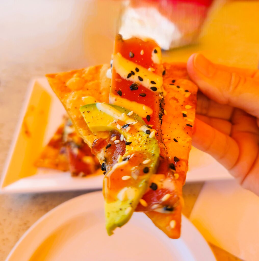 Close up of a bite of Crunchy Seared Tuna and Avocado on a tortilla topped with sauce and sesame seeds.