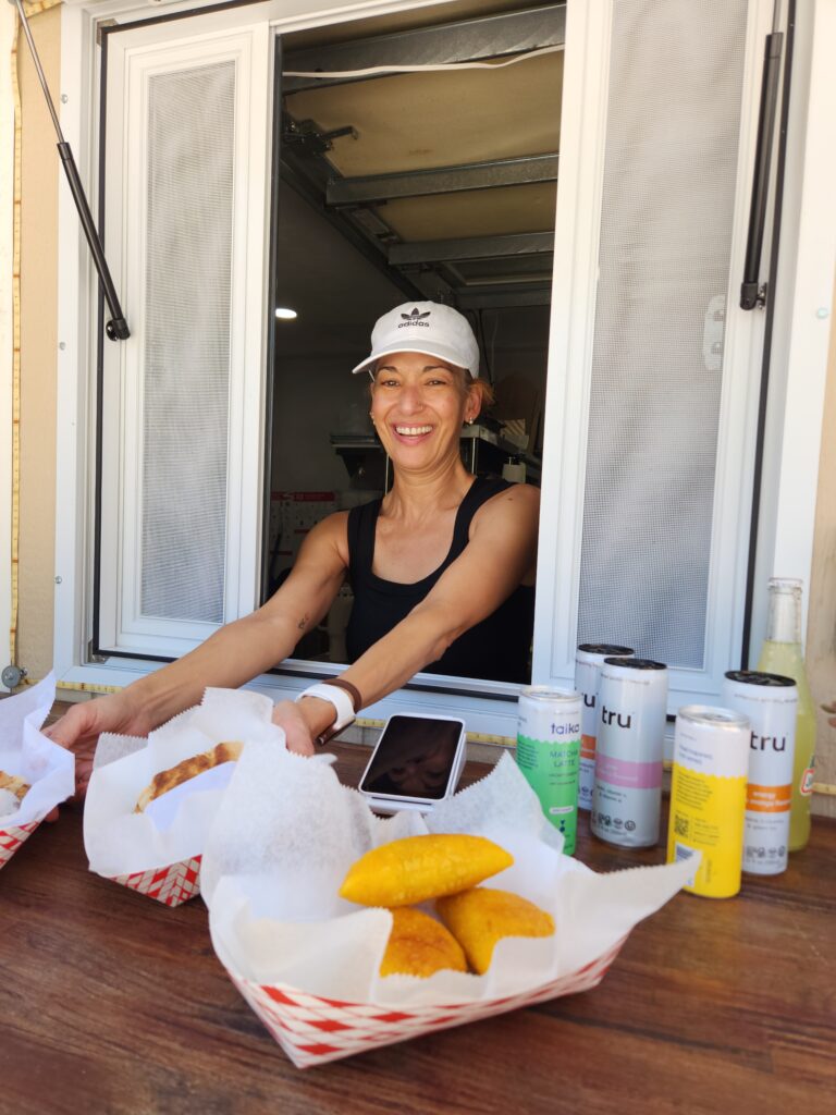A smiling woman handing trays filled with Cuban food out a shop window.