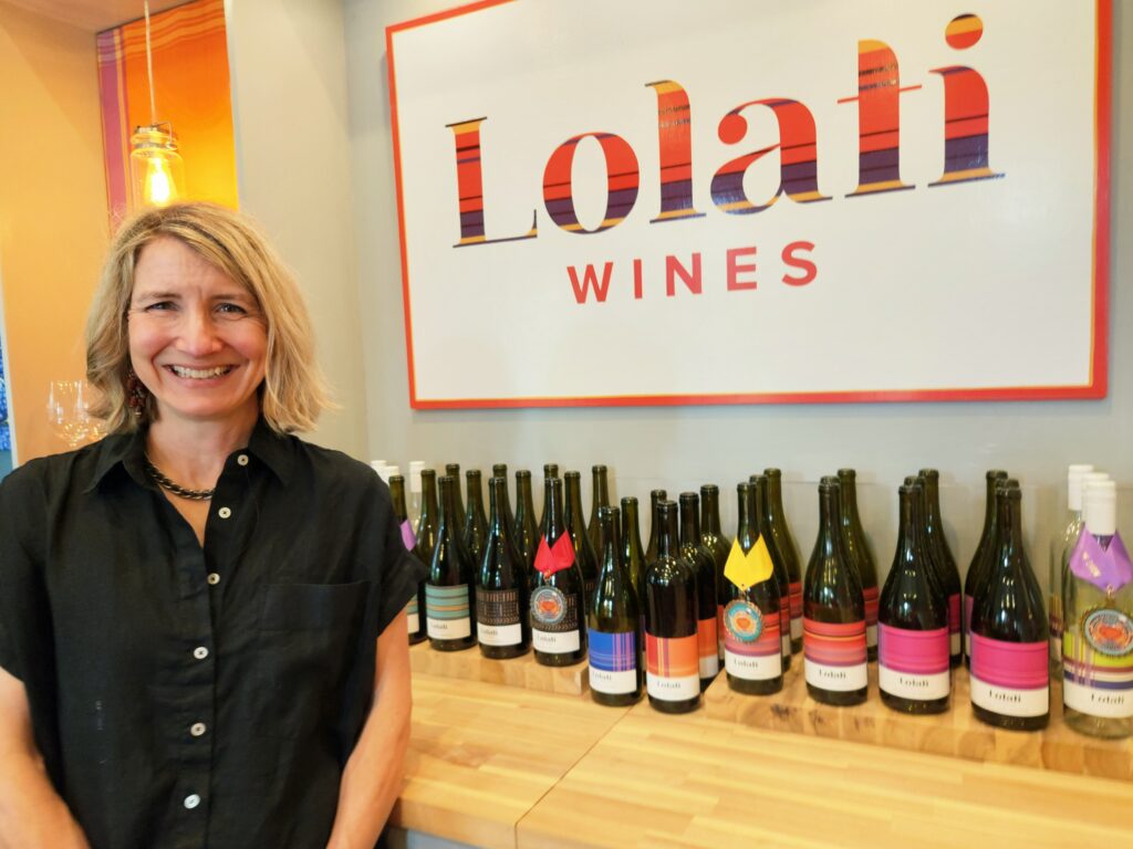 26 Sensational Must-Visit Oregon Wineries in the Willamette Valley 14 A row of bottles of every type of Lolati wine, with the smiling Leigh, owner and winemaker.