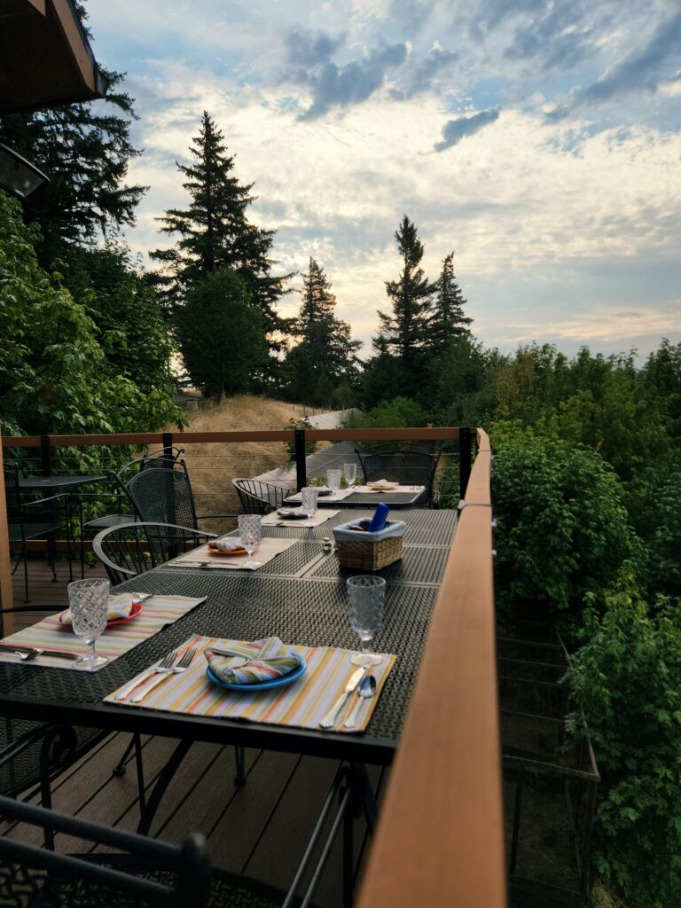 Spend 11 Awesome Days in the Willamette Valley 1 Evergreens and pink sky in the background, with a table set for breakfast on the deck overlooking the Willamette Valley.