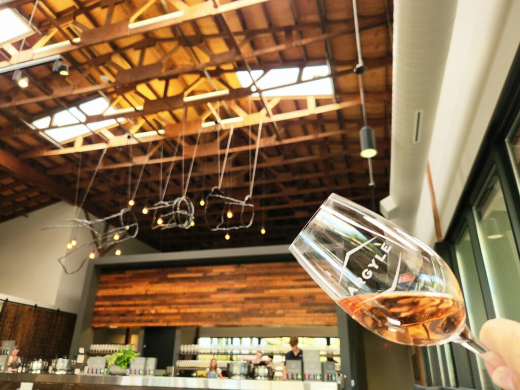 26 Sensational Must-Visit Oregon Wineries in the Willamette Valley 55 A glass of sparkling Rose held at an angle with the tasting room in the background.