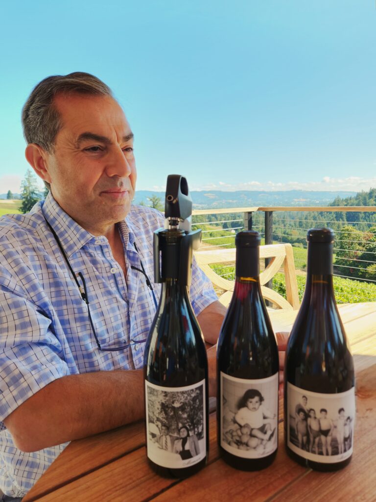 26 Sensational Must-Visit Oregon Wineries in the Willamette Valley 53 A man sitting at a patio table with three bottles of wine that have labels designed from old family photos.