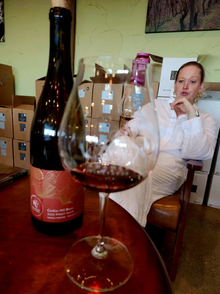 26 Sensational Must-Visit Oregon Wineries in the Willamette Valley 75 Woman sitting in wine storage area talking, with wine and glass on garrel.