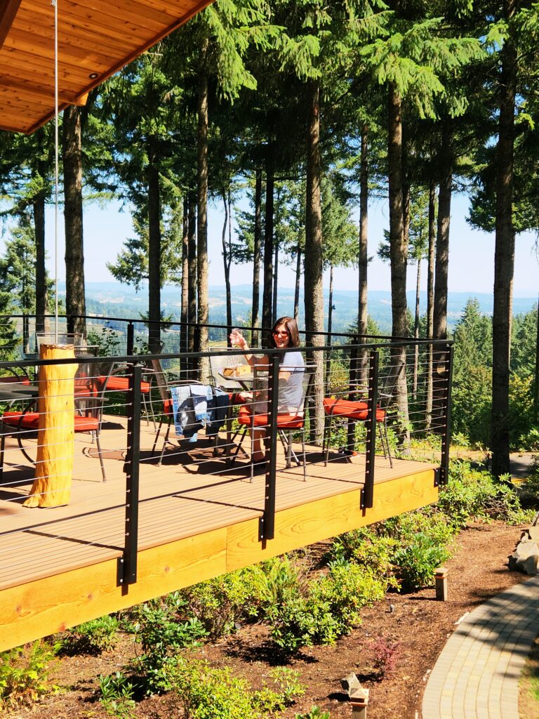 26 Sensational Must-Visit Oregon Wineries in the Willamette Valley 61 A woman sitting at a table on a tree-house style patio high in the tree-tops, overlooking the Willamette Valley.