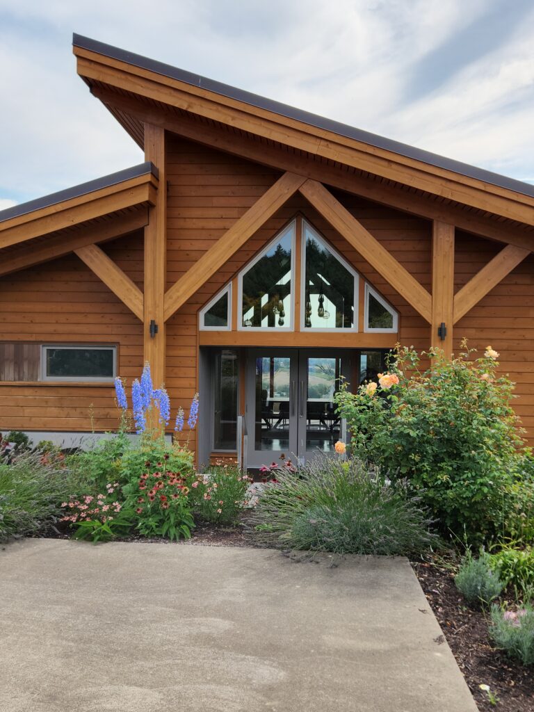 26 Sensational Must-Visit Oregon Wineries in the Willamette Valley 81 A gorgous cedar building with slanted roofline surrounded by wildflowers.