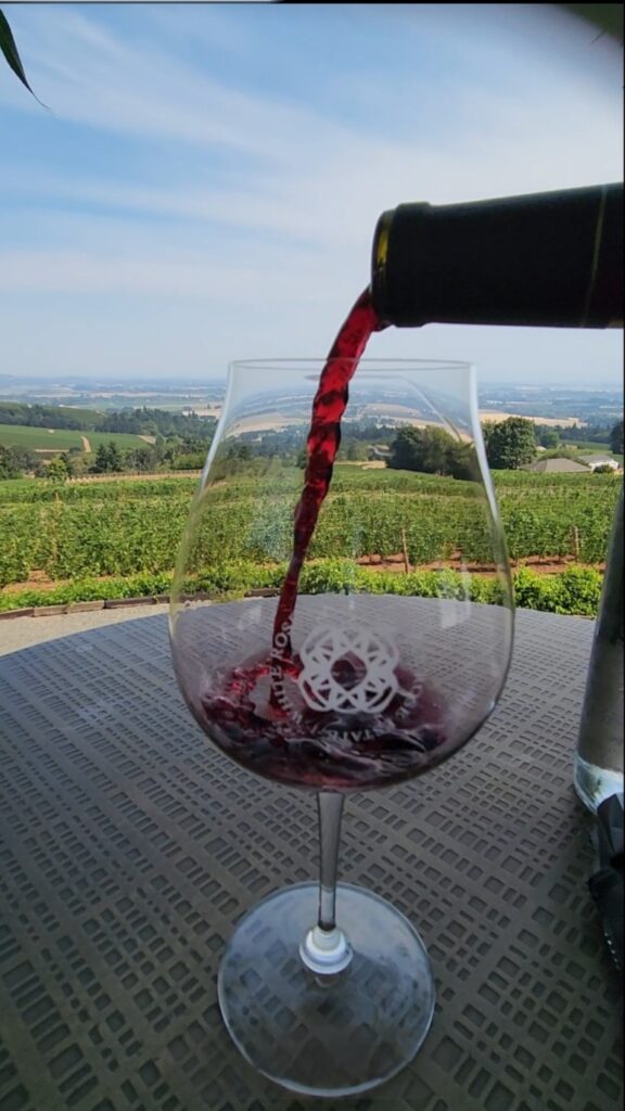 26 Sensational Must-Visit Oregon Wineries in the Willamette Valley 94 A White Rose Estate glass with wine and the Willamette Valley in the background.