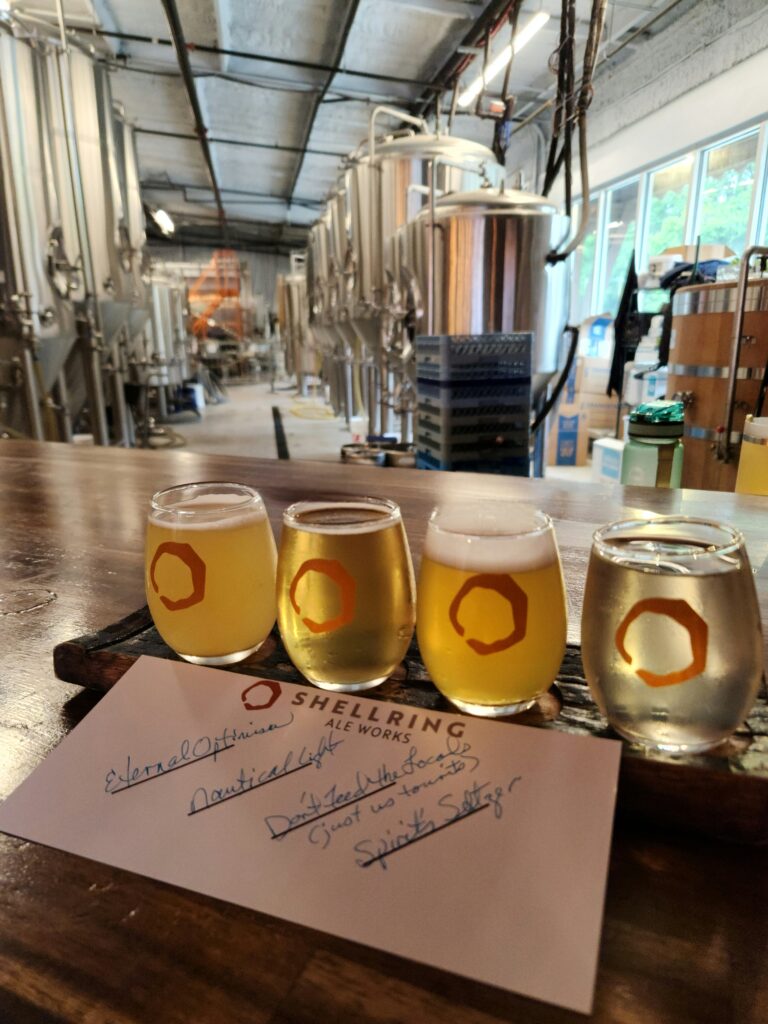 2 Islands, a Lighthouse, & Secret Magic of the Lowcountry 36 A flight of beer (ale) in glasses with the shell ring logo, with stainless tanks in the taproom in the background.