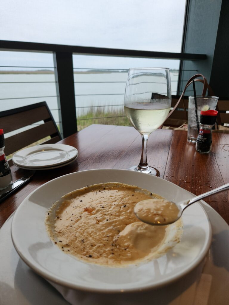 2 Islands, a Lighthouse, & Secret Magic of the Lowcountry 34 A bowl of Lobster Bisque and glass of white wine with water view in background.