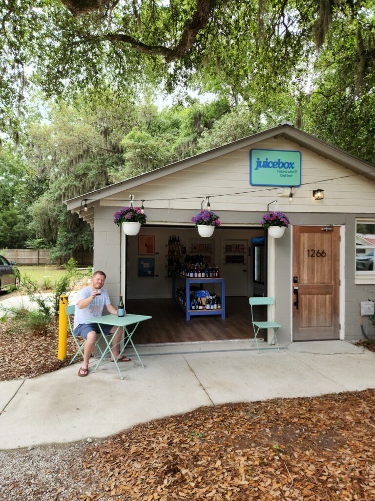 2 Islands, a Lighthouse, & Secret Magic of the Lowcountry 71 The small garage that is the Juicebox Wine store, with the owner enjoying a taste of his wares outside at a tiny patio table.