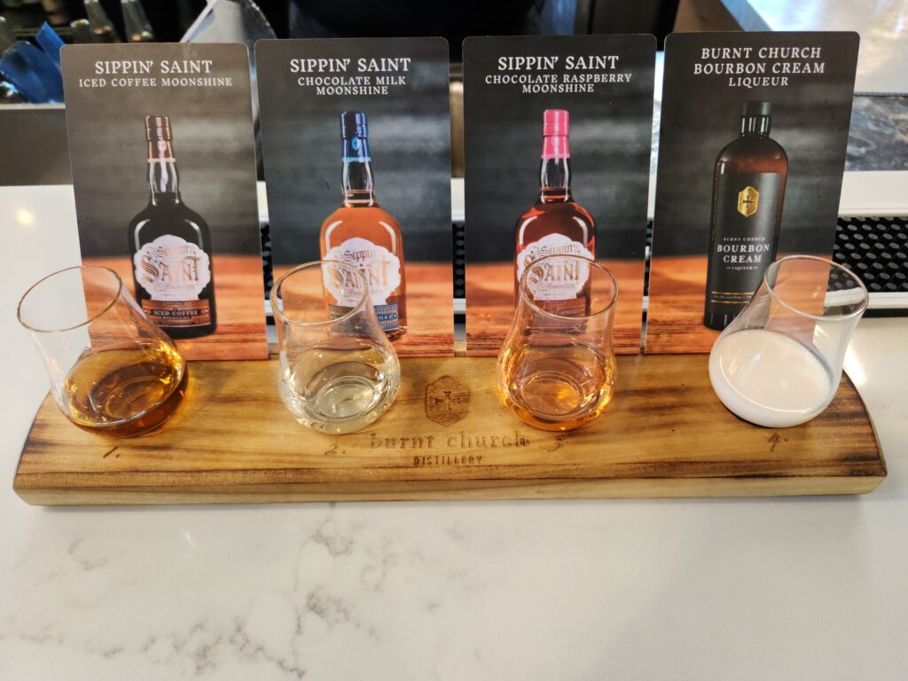 2 Islands, a Lighthouse, & Secret Magic of the Lowcountry 76 A row of shot glasses set up on a wooden holder, with cards showing the type of Moonshine in each glass.