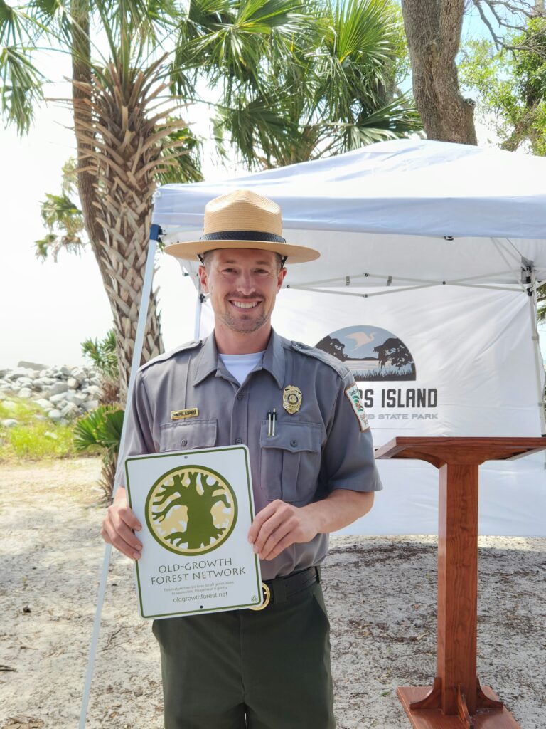2 Islands, a Lighthouse, & Secret Magic of the Lowcountry 30 Man holding sign just awarded to Hunting Island State Park for the designation of Old-Growth Forest Network.
