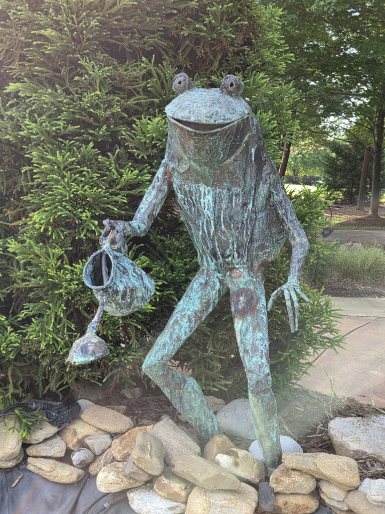Greensboro: Big, Unexpected Adventures From 1781 Battlefield to Jeansboro 6 Large metal sculptures of a frog watering plants in the children's garden.