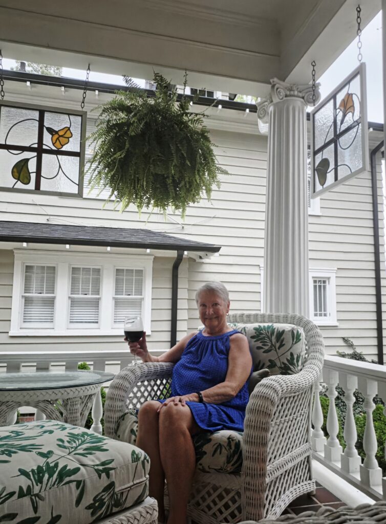 Greensboro: Big, Unexpected Adventures From 1781 Battlefield to Jeansboro 54 Woman (the writer) enjoying a glass of wine on the veranda of the inn, sitting in a white wicker chair with fern print cushion.