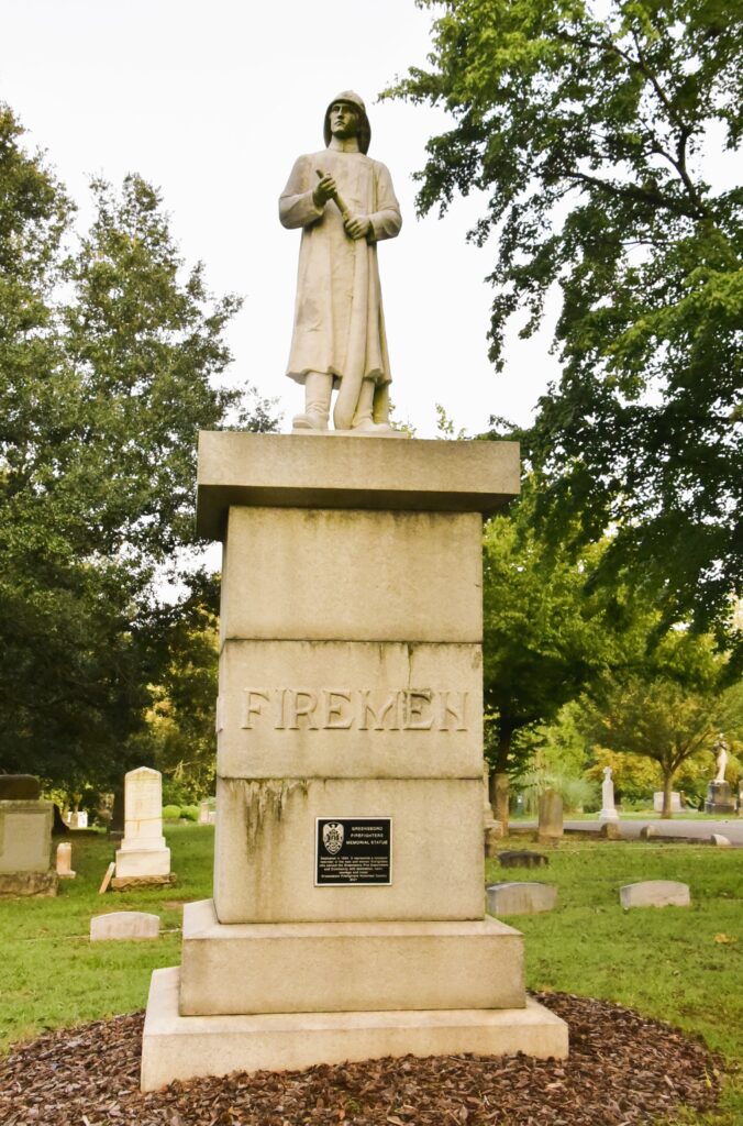 Greensboro: Big, Unexpected Adventures From 1781 Battlefield to Jeansboro 11 Monument to Firemen buried at Green Hill Cemetery--Fireman in old knee-length coat in helmet, holding hose.