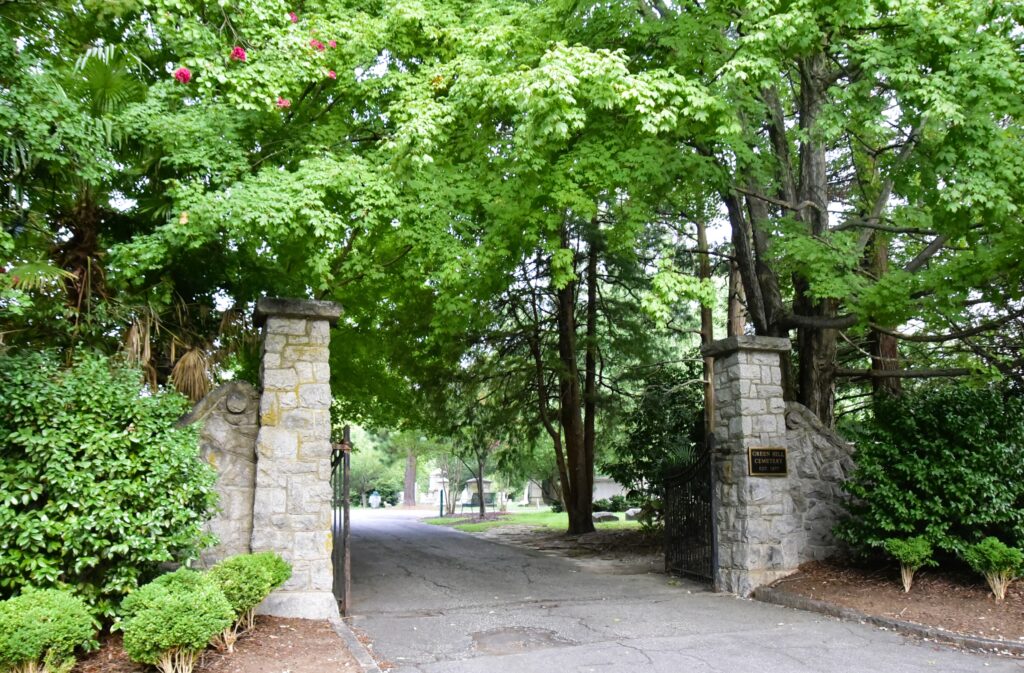 Greensboro: Big, Unexpected Adventures From 1781 Battlefield to Jeansboro 10 Stone entry gate pillars at Green Hill Cemetery, surrounded by trees.