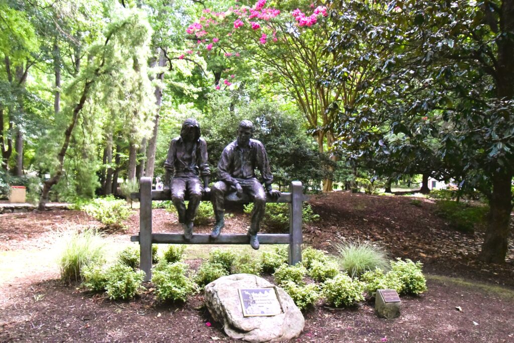 Greensboro: Big, Unexpected Adventures From 1781 Battlefield to Jeansboro 9 Two sculptures of people sitting on a split rail fence in the garden at Greensboro's Tanger Family Bicentennial Garden.